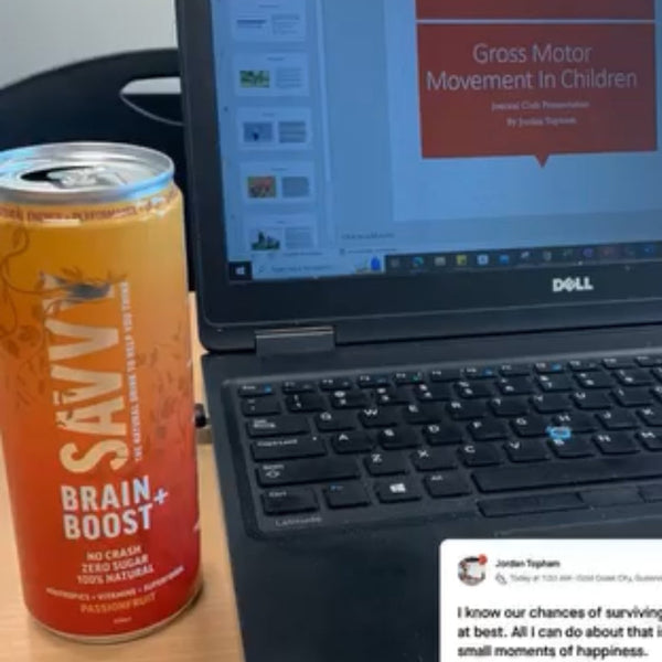 Laptop on a desk with a can of Savvy Brain Boost and a social media post displayed.